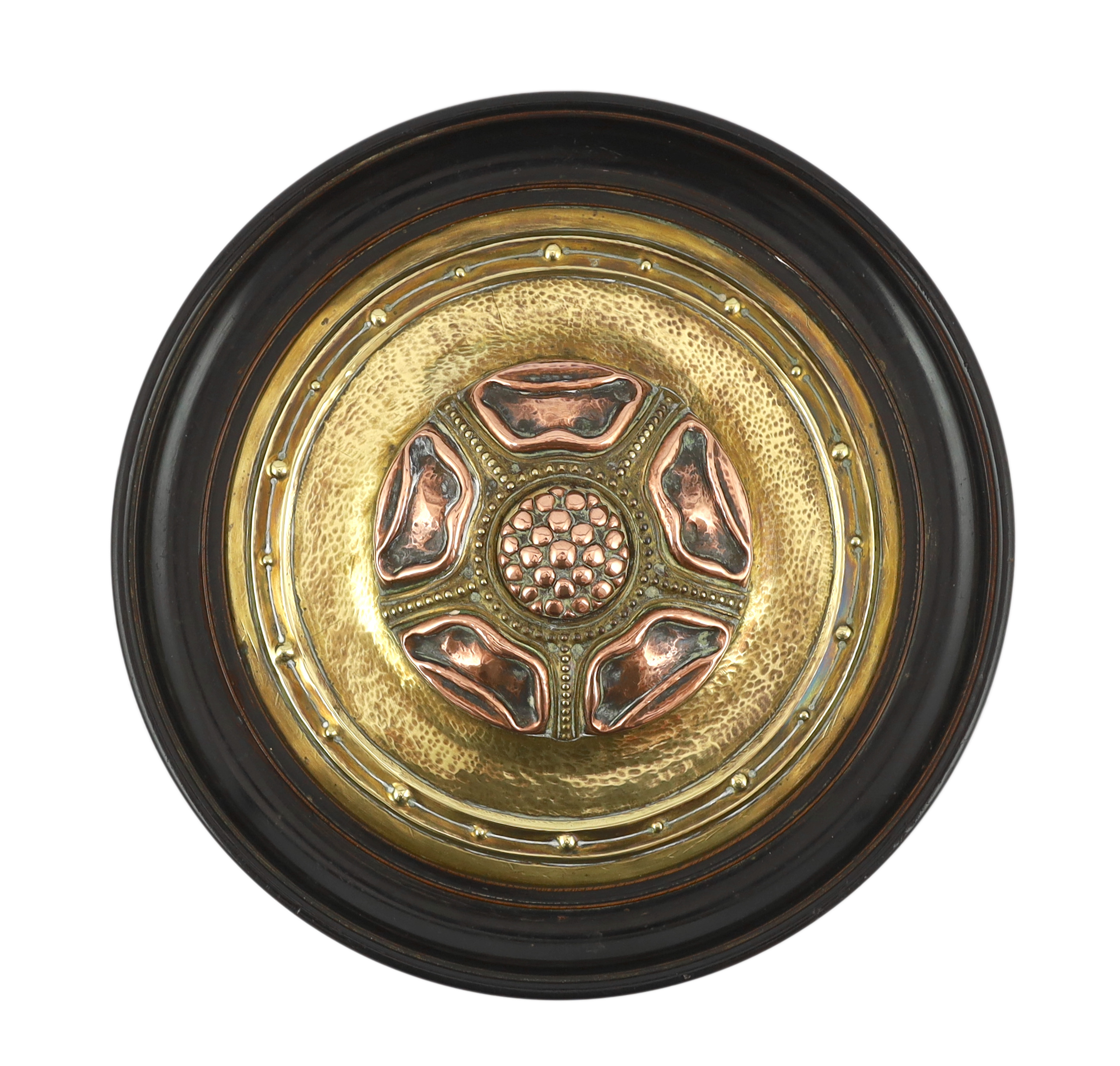 An Arts and Crafts brass and copper roundel, in the manner of Archibald Knox, monogrammed CA, ebony framed, overall 27cm